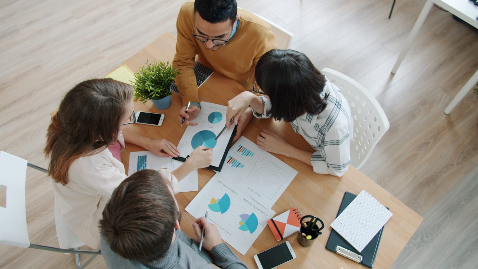 Equipo revisando gráficas impresas alrededor de una mesa.